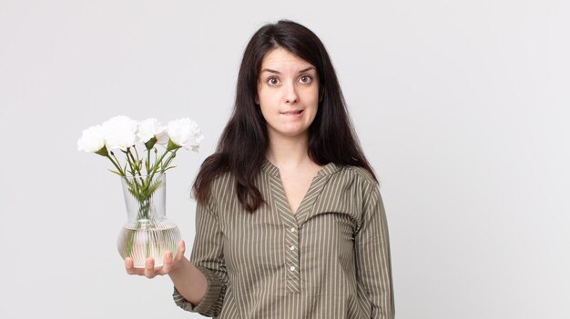 Mujer bonita que parece perpleja y confundida y sostiene flores decorativas. agente asistente con auriculares