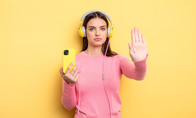 Mujer bonita que parece seria mostrando la palma abierta haciendo un gesto de parada. escuchar música concepto