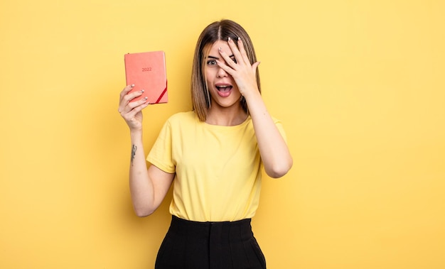 Mujer bonita que parece sorprendida asustada o aterrorizada cubriendo la cara con el concepto de planificador manual