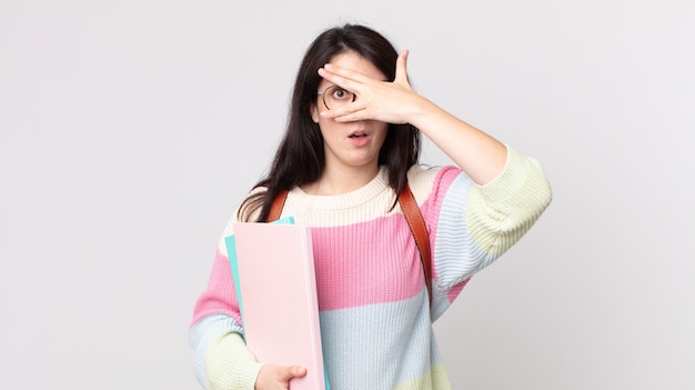 Mujer bonita que parece sorprendida, asustada o aterrorizada, cubriéndose el rostro con la mano. concepto de estudiante universitario