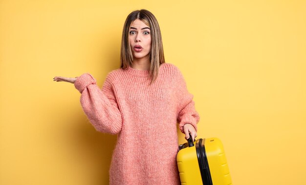 Mujer bonita que parece sorprendida y conmocionada, con la mandíbula caída sosteniendo un objeto. concepto de viaje en maleta