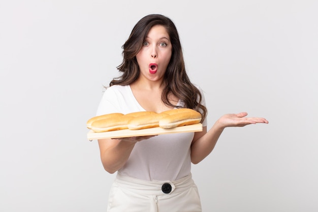 Mujer bonita que parece sorprendida y conmocionada, con la mandíbula caída sosteniendo un objeto y sosteniendo una bandeja de panecillos