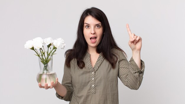 Mujer bonita que se siente como un genio feliz y emocionado después de darse cuenta de una idea y sostener flores decorativas. agente asistente con un auricular