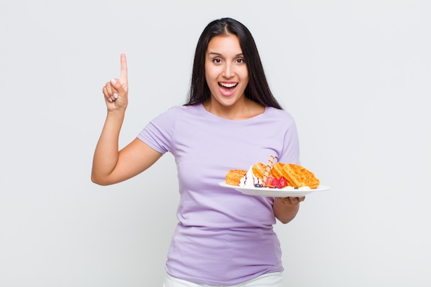 Mujer bonita que se siente como un genio feliz y emocionado después de realizar una idea, levantando alegremente el dedo, ¡eureka!