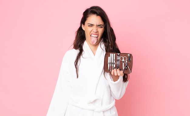 Mujer bonita que se siente disgustada e irritada y con la lengua fuera y sosteniendo una bolsa de maquillaje con herramientas de uñas