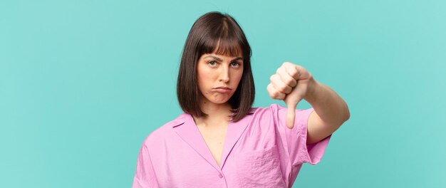 Mujer bonita que se siente enfadada, enojada, molesta, decepcionada o disgustada, mostrando el pulgar hacia abajo con una mirada seria.