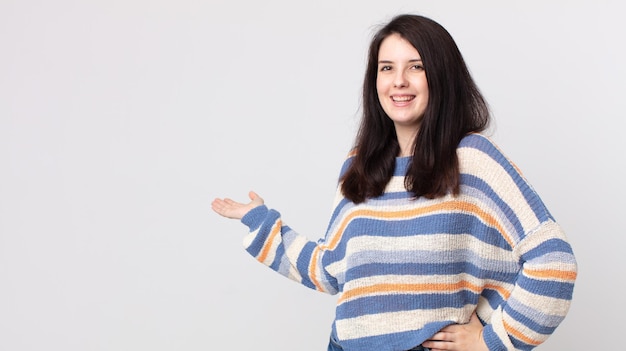 Mujer bonita que se siente feliz y alegre, sonríe y te da la bienvenida, invitándote a entrar con un gesto amistoso