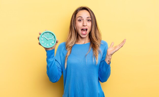 Mujer bonita que se siente feliz y asombrada por algo increíble sosteniendo un despertador