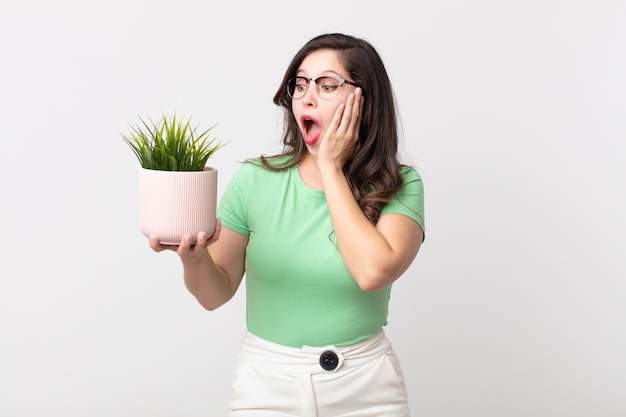 Mujer bonita que se siente feliz, emocionada y sorprendida y sosteniendo una planta decorativa