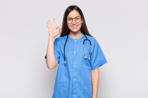 Mujer bonita que se siente feliz, relajada y satisfecha, mostrando aprobación con gesto bien, sonriendo