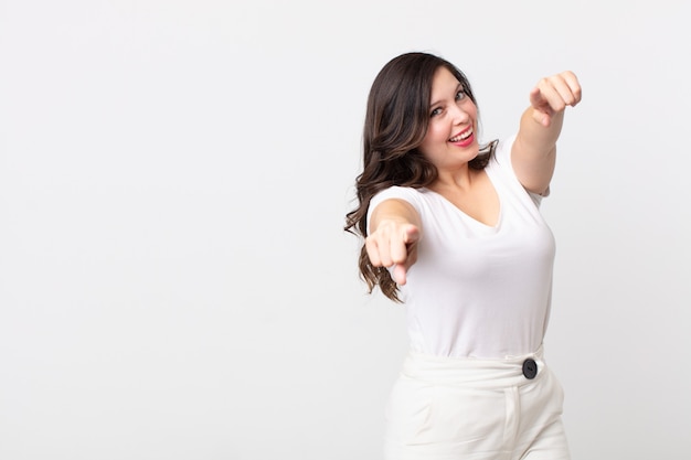 Mujer bonita que se siente feliz y segura, apuntando a la cámara con ambas manos y riendo, eligiéndote