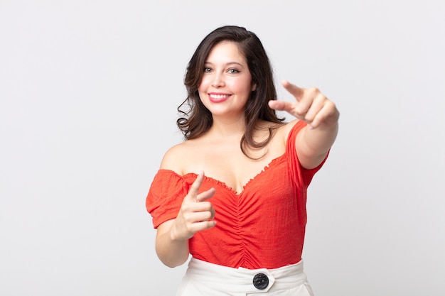 Mujer bonita que se siente feliz y segura, apuntando a la cámara con ambas manos y riendo, eligiéndote