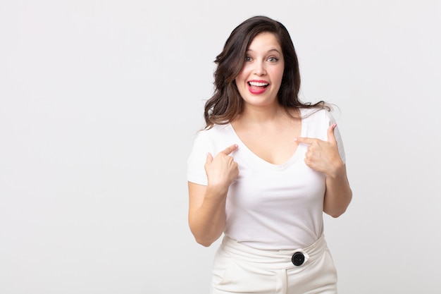 Mujer bonita que se siente feliz, sorprendida y orgullosa, señalando a sí misma con una mirada emocionada y asombrada