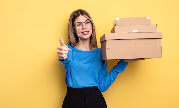 Mujer bonita que se siente orgullosa, sonriendo positivamente con los pulgares arriba concepto de cajas de paquetes