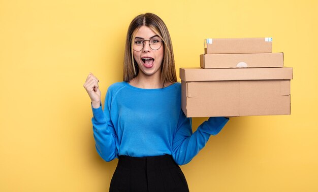 Mujer bonita que se siente sorprendida, riendo y celebrando el concepto de cajas de paquetes de éxito