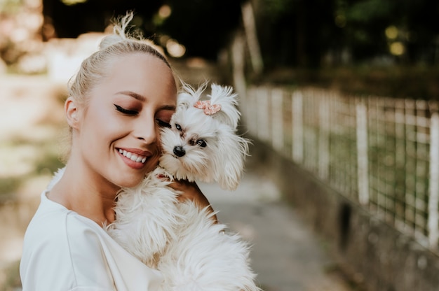 Mujer bonita que sostiene un perro maltés lindo, pequeño.