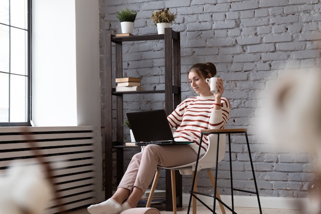 Mujer bonita que trabaja en la oficina moderna con ordenador portátil y tomando café