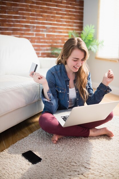 Mujer bonita que usa su tarjeta de crédito para comprar en línea sentada en el piso de la sala de estar