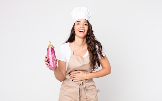 Mujer bonita riendo a carcajadas de una broma hilarante con un delantal y sosteniendo una berenjena