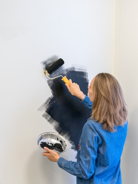 Una mujer bonita con un rodillo pinta la pared de negro. Concepto de reparación de viviendas. Copie el espacio. Vista vertical.