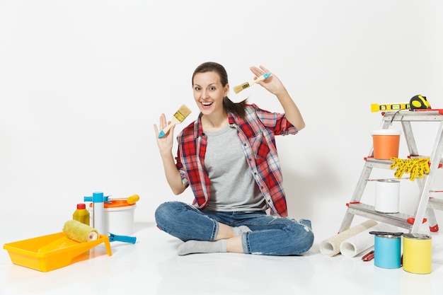 Foto mujer bonita en ropa casual sentada en el piso con cepillo, instrumentos para habitación de apartamento de renovación aislado sobre fondo blanco. accesorios de papel pintado para pegar herramientas de pintura. reparar el concepto de hogar