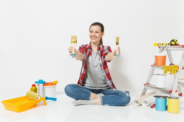 Mujer bonita en ropa casual sentada en el piso con cepillo, instrumentos para habitación de apartamento de renovación aislado sobre fondo blanco. Accesorios de papel pintado para pegar herramientas de pintura. Reparar el concepto de hogar