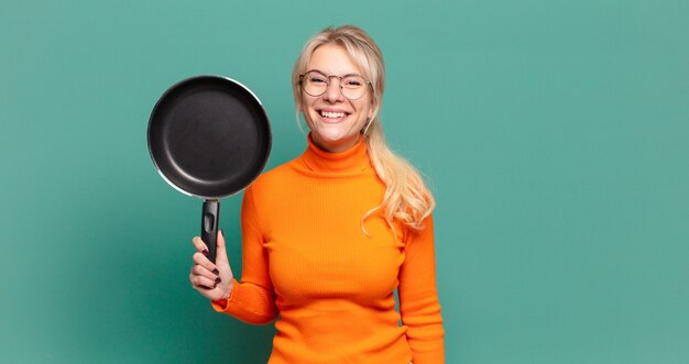 Mujer bonita rubia aprendiendo a cocinar con una sartén