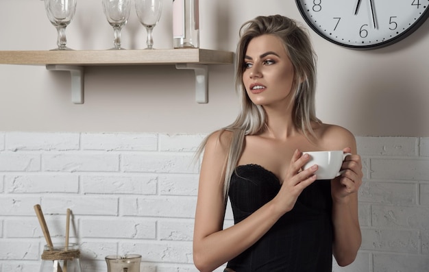 Mujer bonita rubia bebiendo café en la cocina blanca por la mañana con espacio para copiar