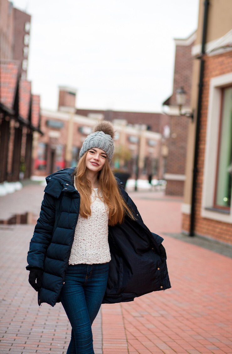 Mujer bonita rubia con gorro de punto y abrigo posando cerca del centro comercial