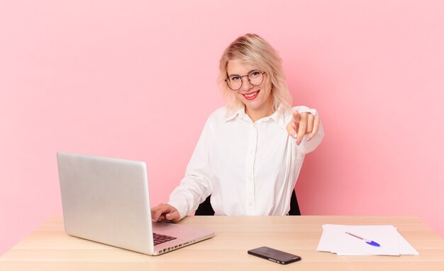 Mujer bonita rubia joven mujer bonita apuntando a la cámara eligiéndote. concepto de escritorio de espacio de trabajo