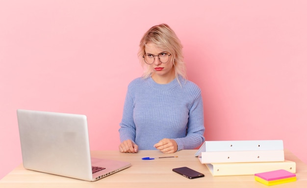 Mujer bonita rubia joven mujer bonita que se siente triste, molesta o enojada y mirando hacia un lado. concepto de escritorio de espacio de trabajo