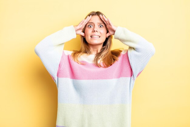 Mujer bonita rubia levantando las manos a la cabeza, con la boca abierta, sintiéndose extremadamente afortunada, sorprendida, emocionada y feliz