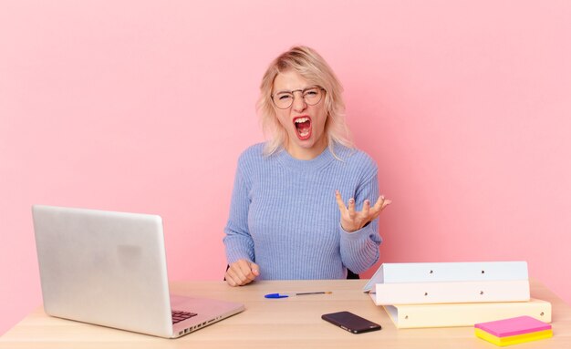 Mujer bonita rubia mujer bonita joven que parece enojada, molesta y frustrada. concepto de escritorio de espacio de trabajo