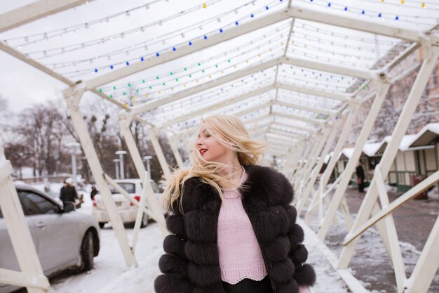 Mujer bonita rubia con el pelo en movimiento posando en la calle con nieve