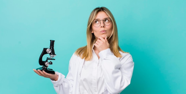 Mujer bonita rubia pensando sintiéndose dudosa y confundida científico y concepto de microscopio