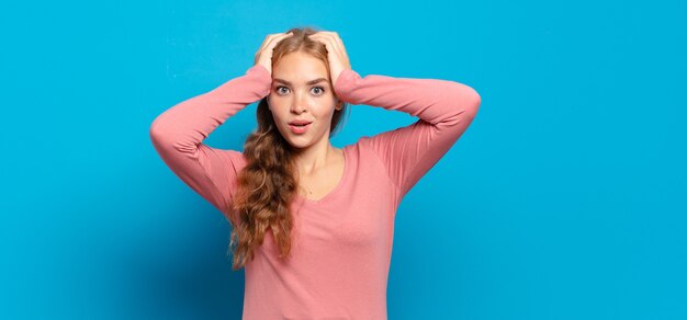 Mujer bonita rubia que parece emocionada y sorprendida, con la boca abierta con ambas manos en la cabeza, sintiéndose como una ganadora afortunada