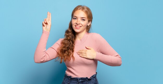 Mujer bonita rubia que parece feliz, segura y digna de confianza, sonriendo y mostrando el signo de la victoria, con una actitud positiva