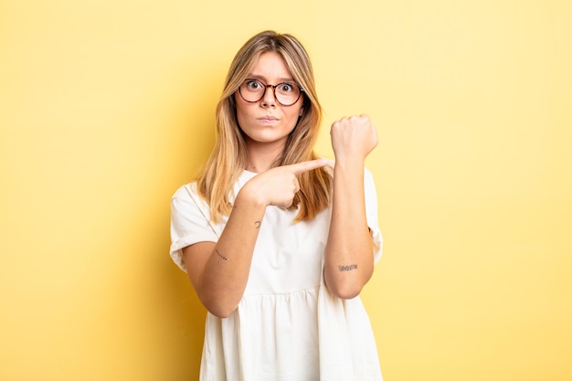 Mujer bonita rubia que parece impaciente y enojada, señalando el reloj, pidiendo puntualidad, quiere llegar a tiempo