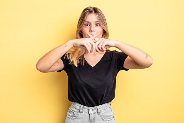 Mujer bonita rubia que parece seria y disgustada con ambos dedos cruzados al frente en rechazo, pidiendo silencio