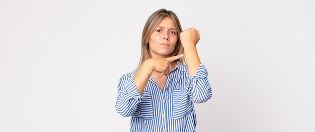 Mujer bonita rubia que parece somnolienta, aburrida y bostezando, con dolor de cabeza y una mano cubriendo la mitad de la cara