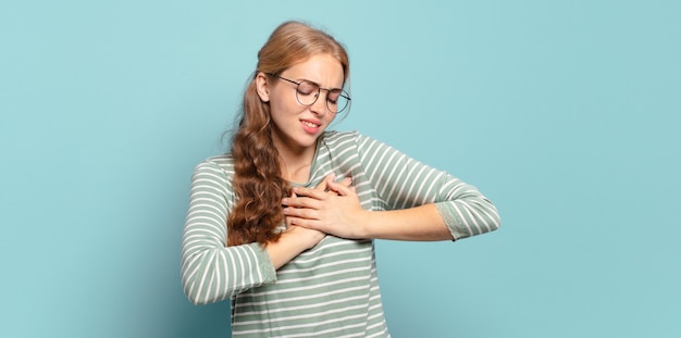 Mujer bonita rubia que parece triste, herida y desconsolada, sosteniendo ambas manos cerca del corazón, llorando y sintiéndose deprimida