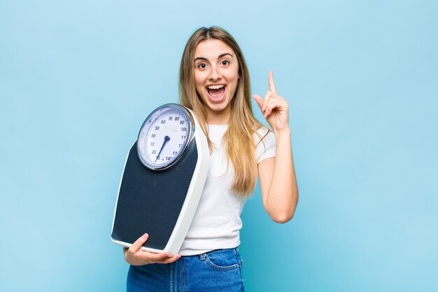 Mujer bonita rubia que se siente como un genio feliz y emocionado después de realizar una idea, levantando alegremente el dedo, ¡eureka!