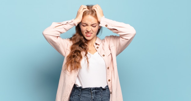 Mujer bonita rubia que se siente estresada y frustrada, levantando las manos a la cabeza, sintiéndose cansada, infeliz y con migraña