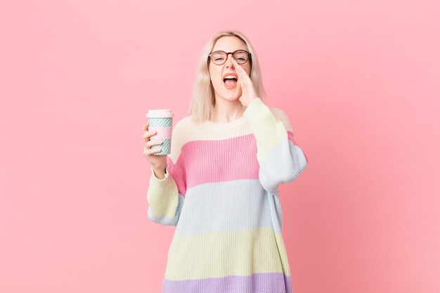 Mujer bonita rubia que se siente feliz, dando un gran grito con las manos al lado de la boca. concepto de cafe