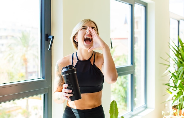 Mujer bonita rubia que se siente feliz, emocionada y positiva, dando un gran grito con las manos al lado de la boca, gritando