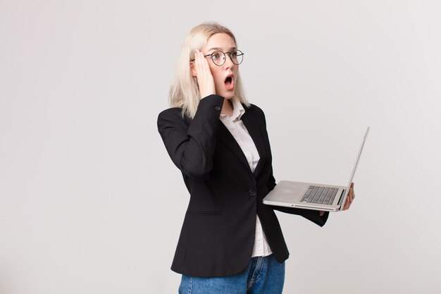 Mujer bonita rubia que se siente feliz, emocionada y sorprendida y sosteniendo una computadora portátil