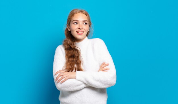 Mujer bonita rubia que se siente feliz, orgullosa y esperanzada, preguntándose o pensando, mirando hacia arriba para copiar el espacio con los brazos cruzados