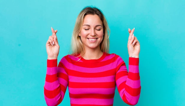 Mujer bonita rubia que se siente nerviosa y esperanzada cruzando los dedos rezando y esperando buena suerte