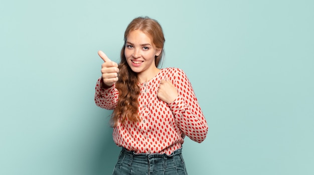 Mujer bonita rubia que se siente orgullosa, despreocupada, segura y feliz, sonriendo positivamente con los pulgares hacia arriba