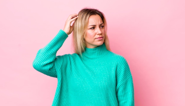 Mujer bonita rubia que se siente perpleja y confundida rascándose la cabeza y mirando hacia un lado